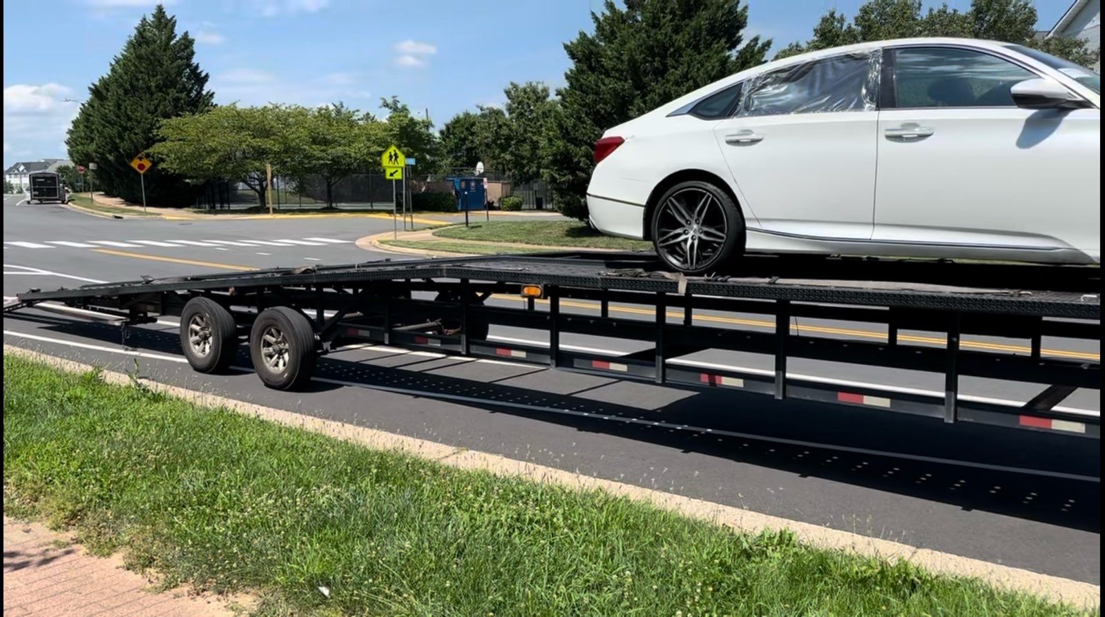Flatbed pickup — white sedan secured for local delivery.